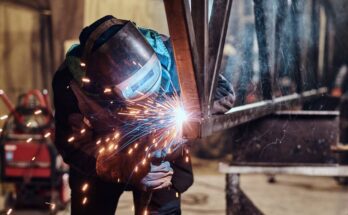 person in a welding suit and helmet welding some metal with sparks flying in a metal fabrication warehouse
