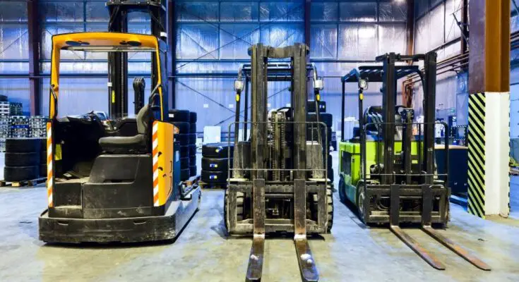 A row of forklifts sitting in a warehouse, each using a variety of power sources from electric to propane.