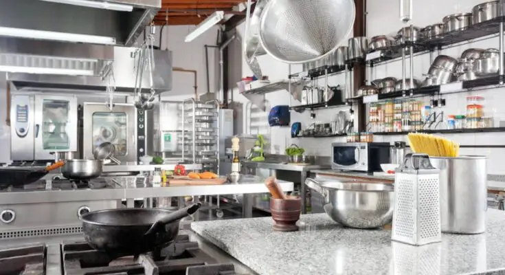 A professional kitchen with a variety of equipment, including colanders, a cast iron pan, dozens of pots, and a cheese grater.