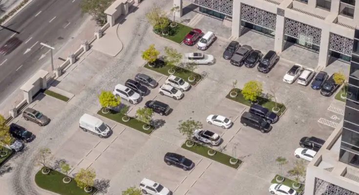 An aerial shot of an incredibly clean commercial parking lot shows many cars parked in various parking spots.