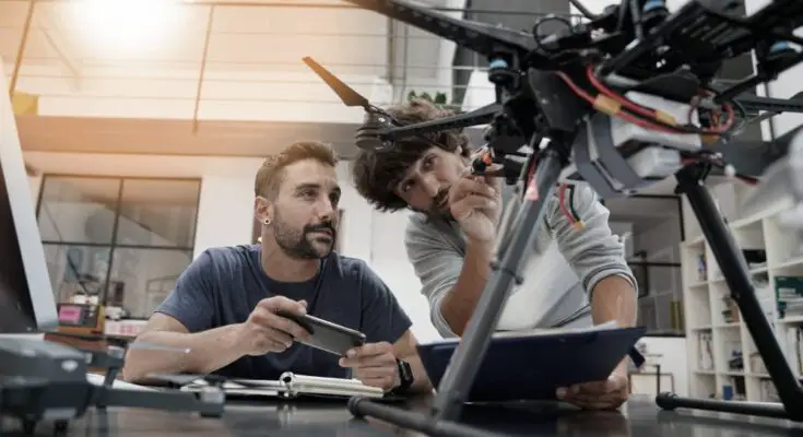 Two engineers in their large office working together as they inspect the mechanics of a drone that sits on their desk.