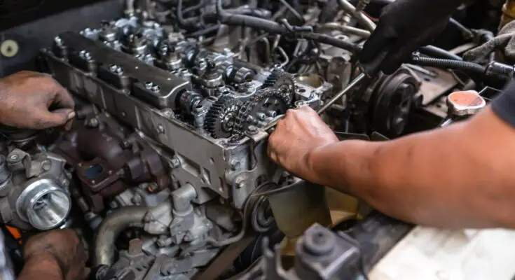 Two mechanics working on various parts of a diesel engine. One is using a tool to perform maintenance on the engine.