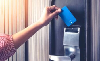 A woman's hand inserting a blue magnetic-strip card key into a reader on a hotel room's door for entry.