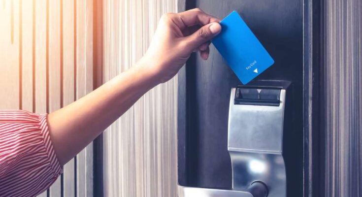 A woman's hand inserting a blue magnetic-strip card key into a reader on a hotel room's door for entry.