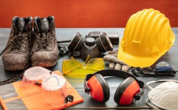 Work safety protection equipment, including hard hats and goggles, laid out on a wooden table against a red background.