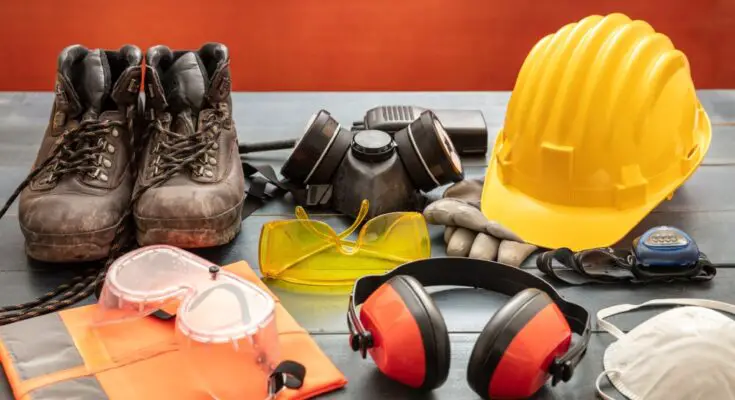 Work safety protection equipment, including hard hats and goggles, laid out on a wooden table against a red background.