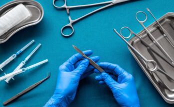 Doctor's hands holding a scalpel with surgical tools arranged on a blue background as he prepares for surgery.