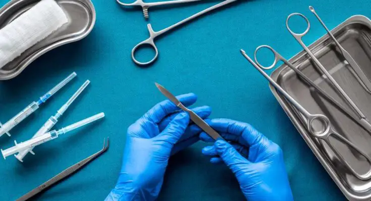 Doctor's hands holding a scalpel with surgical tools arranged on a blue background as he prepares for surgery.