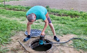 A man in casual clothing pumping sewage waste from a septic tank with a wastewater pump through the maintenance hole.