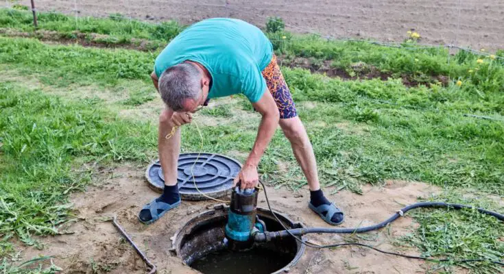 A man in casual clothing pumping sewage waste from a septic tank with a wastewater pump through the maintenance hole.