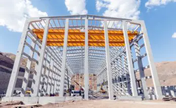 A large metal structure in the process of being built. There are various construction vehicles and materials around it.