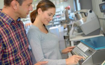 A man and a woman looking at and touching a small industrial scale with multiple functions and a large platform inside a store.