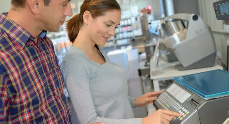 A man and a woman looking at and touching a small industrial scale with multiple functions and a large platform inside a store.