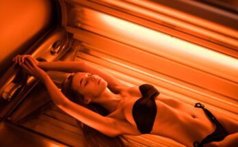 A young woman wearing a bikini, lying with her arms above her head in a tanning bed with orange lights on.