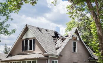 A house surrounded by trees and clouds is the victim to fire damage. The roof is caved in at parts because of the damage.