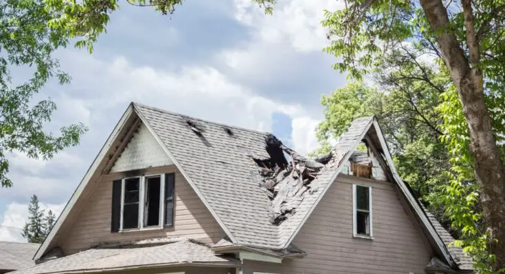 A house surrounded by trees and clouds is the victim to fire damage. The roof is caved in at parts because of the damage.