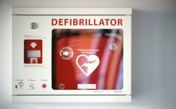 A white steel box with a glass front displays the words defibrillator and holds a red defibrillator.