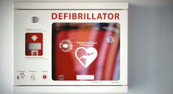 A white steel box with a glass front displays the words defibrillator and holds a red defibrillator.