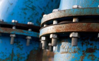 A pair of blue pipelines run next to each other, featuring rust on the outside. Nuts and bolts hold them together.