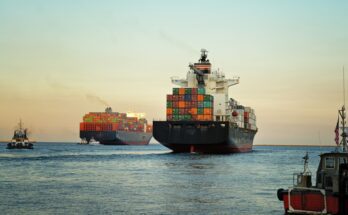 A large container ship at sea with stacks of cargo containers. There's a second container ship in the background.