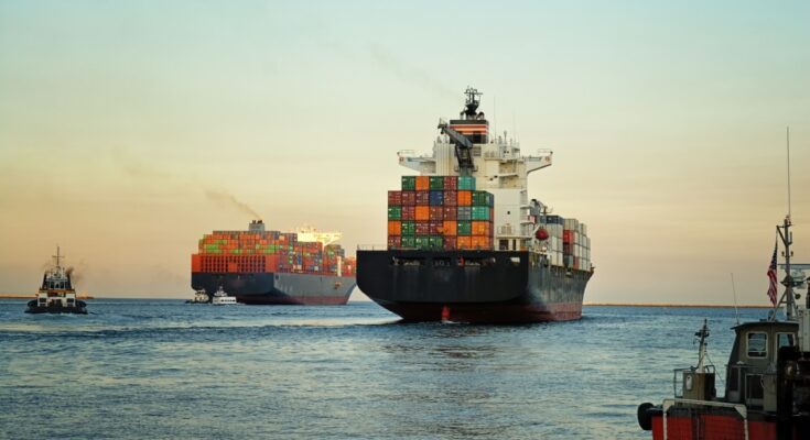 A large container ship at sea with stacks of cargo containers. There's a second container ship in the background.