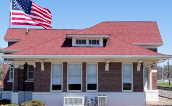 A red brick home with a red roof and many exterior windows with a large flagpole and American flag flying behind it.