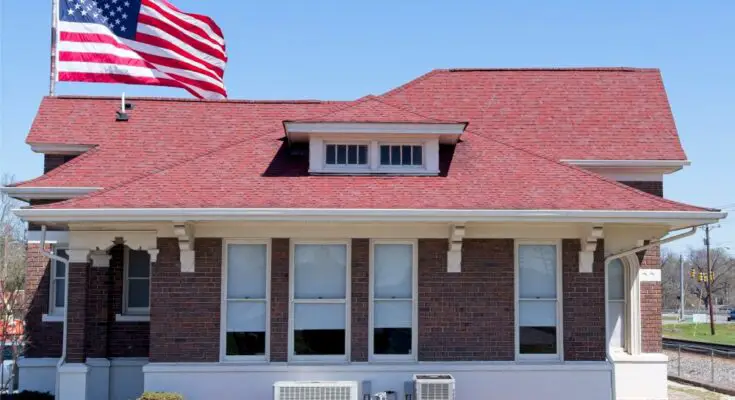 A red brick home with a red roof and many exterior windows with a large flagpole and American flag flying behind it.