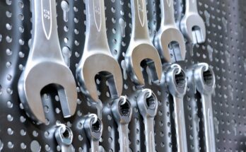 A collection of manual wrenches and spanners placed in ascending order of size on a black pegboard.