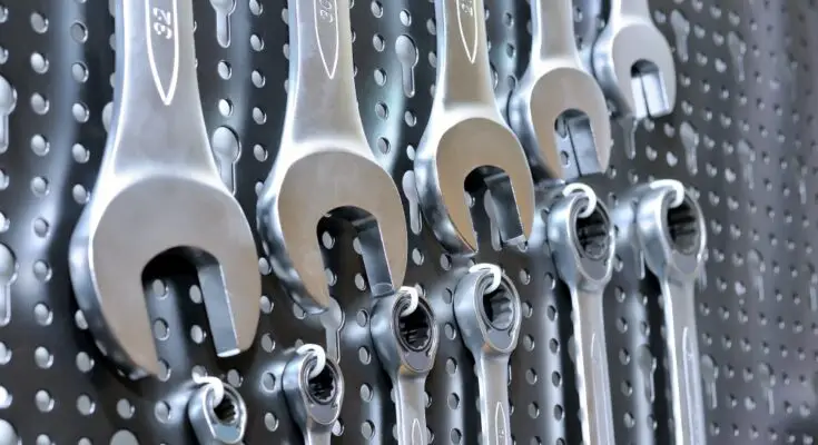 A collection of manual wrenches and spanners placed in ascending order of size on a black pegboard.