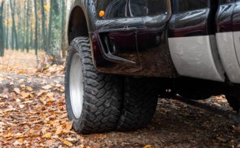 The large front driver's side wheel on an extra-large pickup truck is visible. The setting is an autumnal scene.