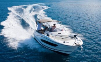 A man driving a high speed motorboat on the open ocean with a sun cover overhead and a large wake behind him.