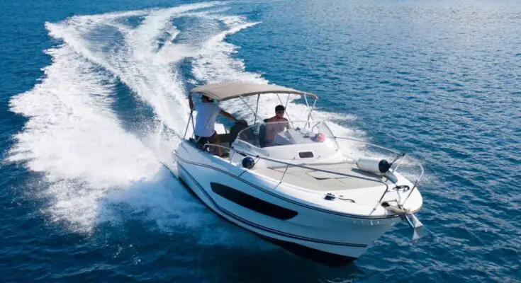 A man driving a high speed motorboat on the open ocean with a sun cover overhead and a large wake behind him.