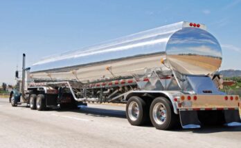 A standard tanker trailer with a sturdy stainless steel body hauling a liquid material. The trailer is on the highway.