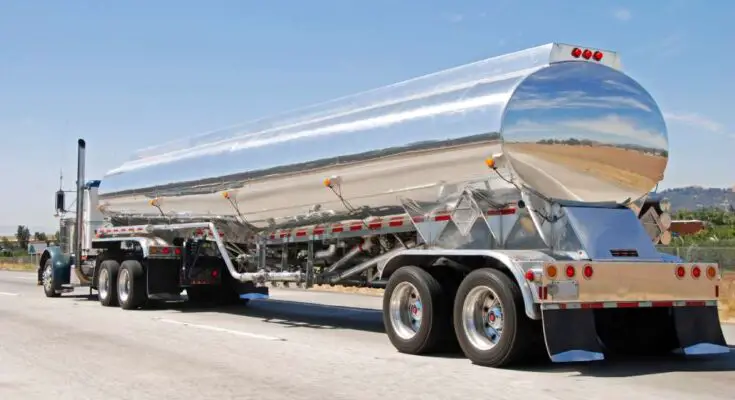 A standard tanker trailer with a sturdy stainless steel body hauling a liquid material. The trailer is on the highway.