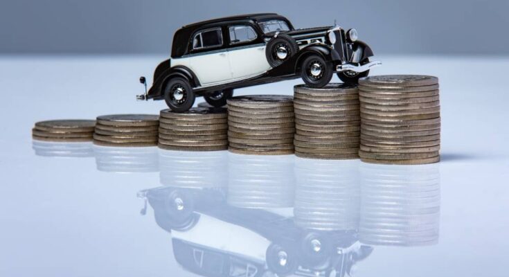 A black-and-white classic car stands on top of a stack of coins, and its reflection appears underneath the table.