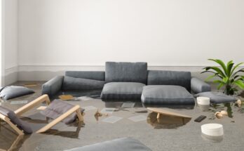 A living room is flooded and all the furniture floats in the water, including a chair, couch cushions, and a remote.