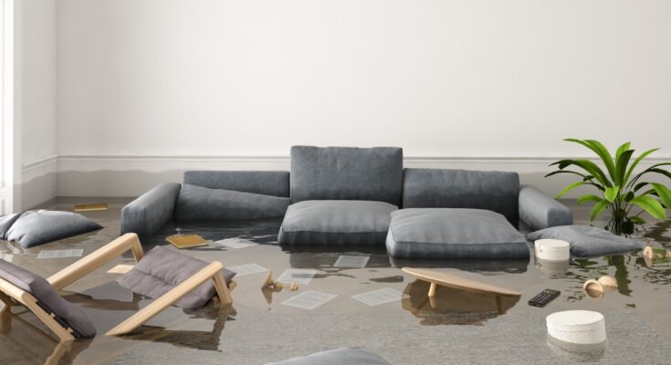 A living room is flooded and all the furniture floats in the water, including a chair, couch cushions, and a remote.