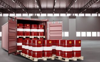 An open red shipping container is inside a warehouse. The container is full of red metal barrels labeled "flammable."