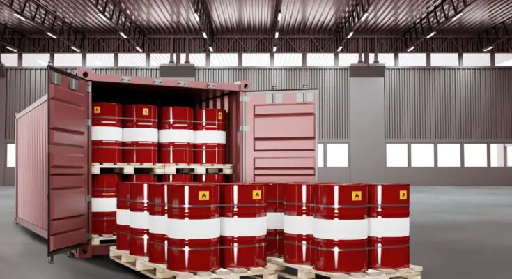 An open red shipping container is inside a warehouse. The container is full of red metal barrels labeled "flammable."