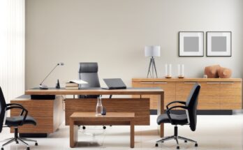 A private office with a wooden desk and coffee table. One black chair is behind the desk and two black chairs are in front of it.