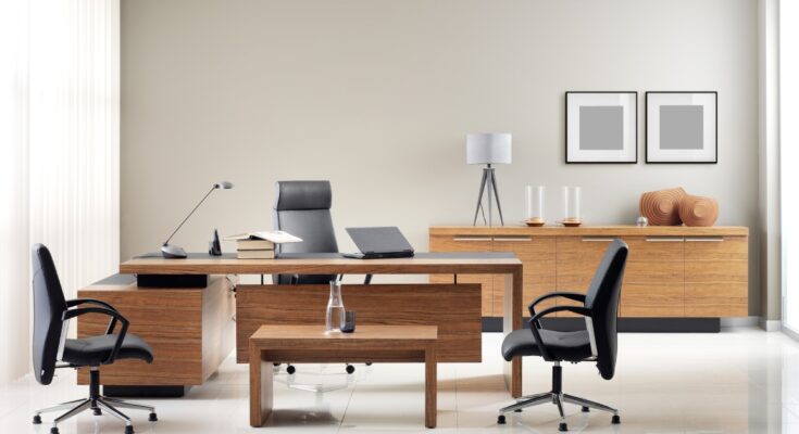 A private office with a wooden desk and coffee table. One black chair is behind the desk and two black chairs are in front of it.