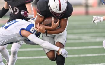 Two football teams playing against each other—a home player rushes with the ball as two opposing players attempt a tackle.