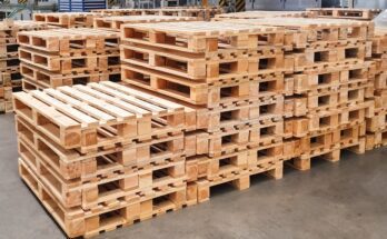 Wooden pallets stacked neatly in a warehouse facility. There are several rows with stacks about five to seven pallets high.