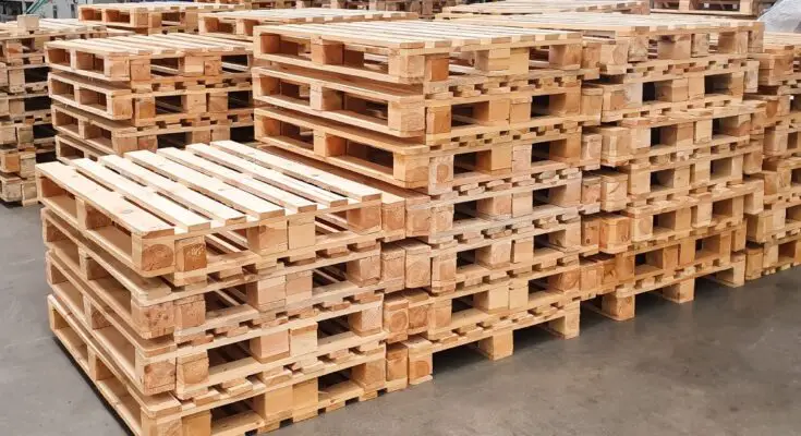 Wooden pallets stacked neatly in a warehouse facility. There are several rows with stacks about five to seven pallets high.