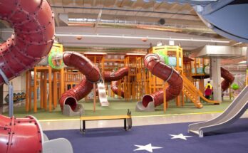 An indoor playground with numerous red metal slides with a spiral curvature and dark-blue rubber surface for flooring.