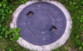 A septic tank with a lid on it. It is positioned near grass and other types of green plants.