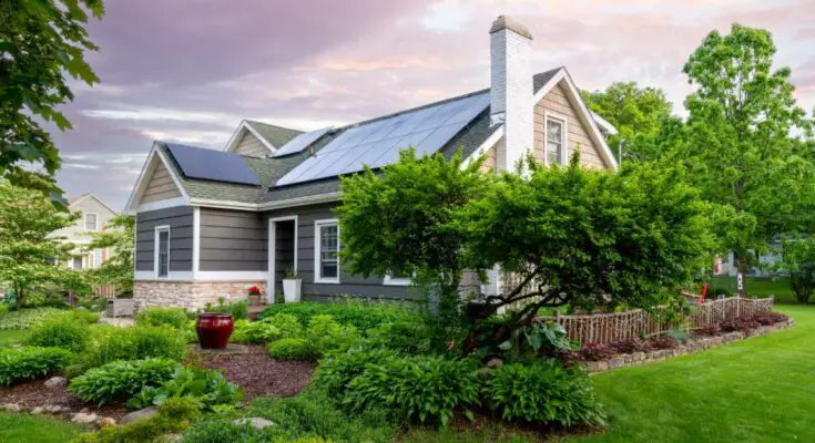 A beautiful East Coast-style residential home with roof-installed solar panels. The house is surrounded by lush landscaping.