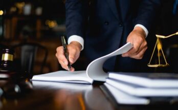 A lawyer in a dark-colored suit is opening a large notebook and using a fancy pen to write something in it.