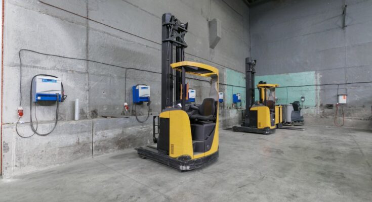 A warehouse storage area with a few forklifts parked off to the sides. There are chargers mounted on the wall.