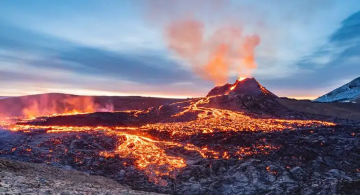 A volcanic eruption with red and orange lava flowing through rocky terrain. Smoke is coming out of the top of the volcano.